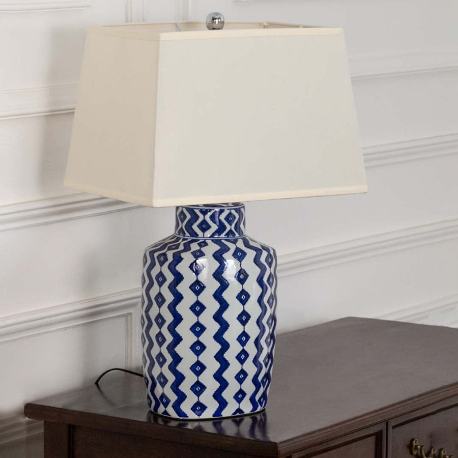 White shade blue patterned ceramic table lamp on wooden sideboard with light off for classic decorative home décor.