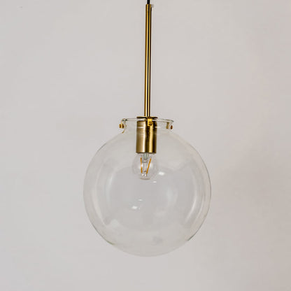 Glass globe pendant light on white background with light off showing clear round glass design and brass fitting.