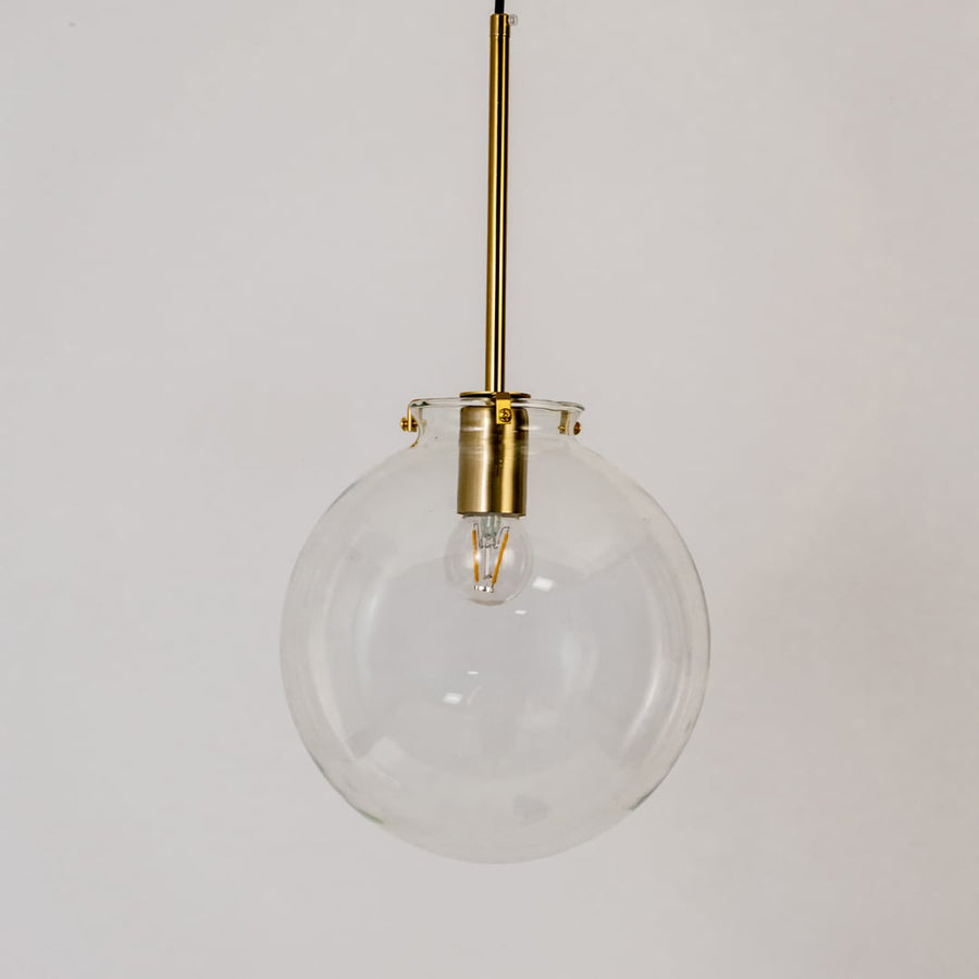 Glass globe pendant light on white background with light off showing clear round glass design and brass fitting.
