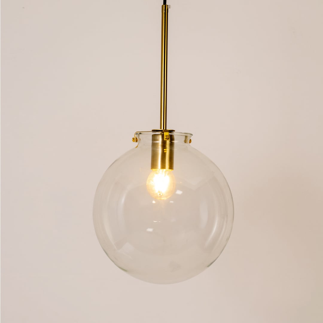 Glass globe pendant light glowing on white background highlighting its transparent glass shade and golden rod.