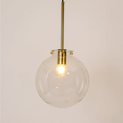 Glass globe pendant light glowing on white background highlighting its transparent glass shade and golden rod.