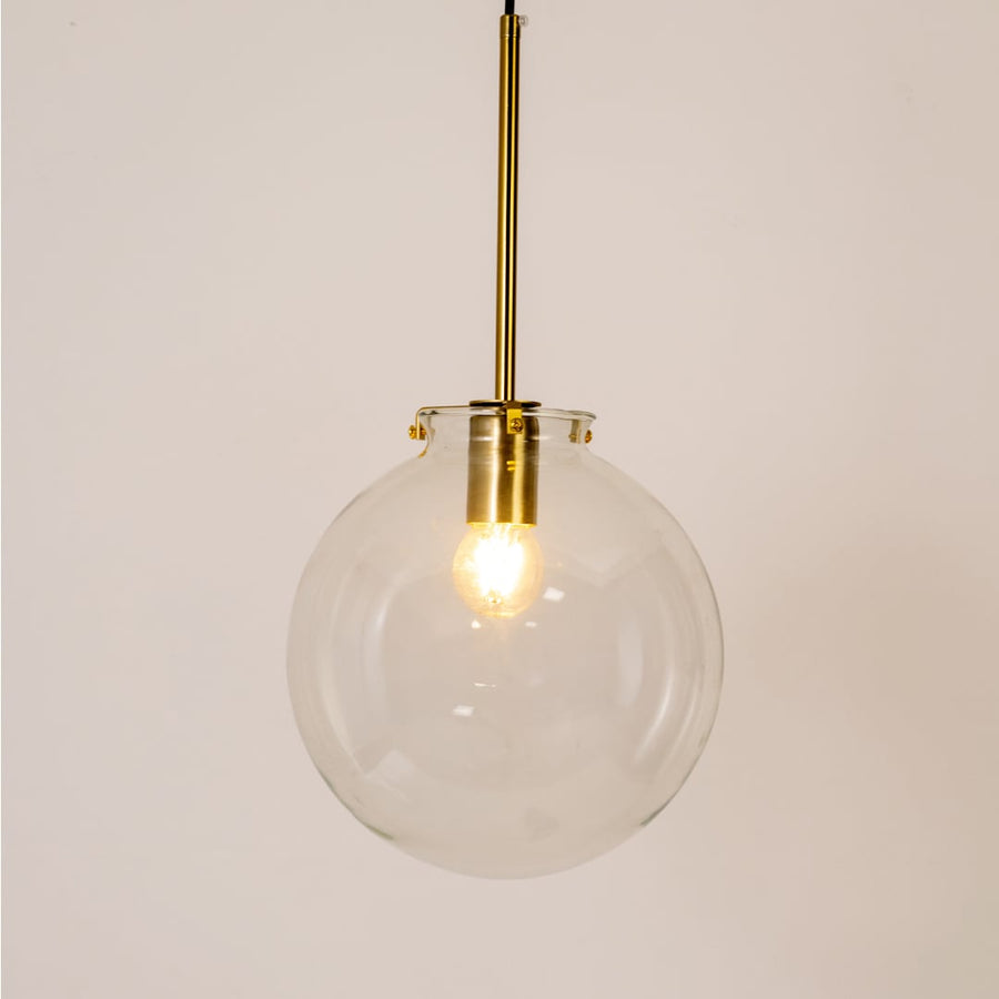 Glass globe pendant light glowing on white background highlighting its transparent glass shade and golden rod.