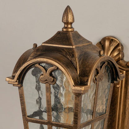 Closeup of gold metal outdoor wall lantern with frosted glass panels and curved arm detailing for sophisticated exterior wall lighting.