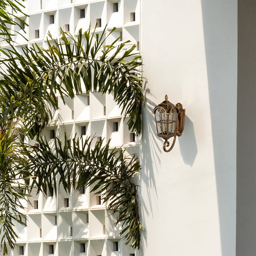 Gold metal outdoor wall lantern with warm light on enhancing the exterior wall and garden view for premium outdoor lighting decor.