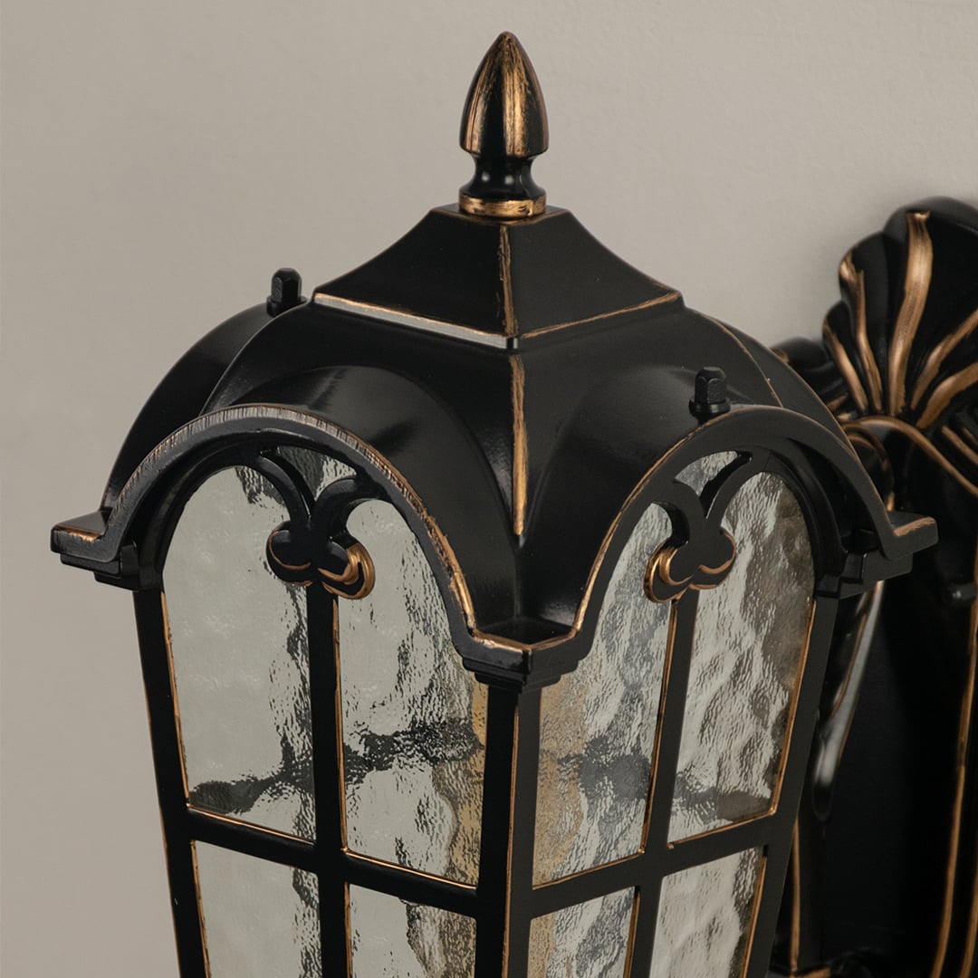 Black metal outdoor wall light closeup image with textured water glass shade and vintage gold edge trim for decor.