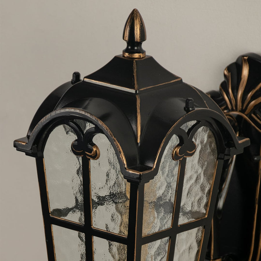 Black metal outdoor wall light closeup image with textured water glass shade and vintage gold edge trim for decor.