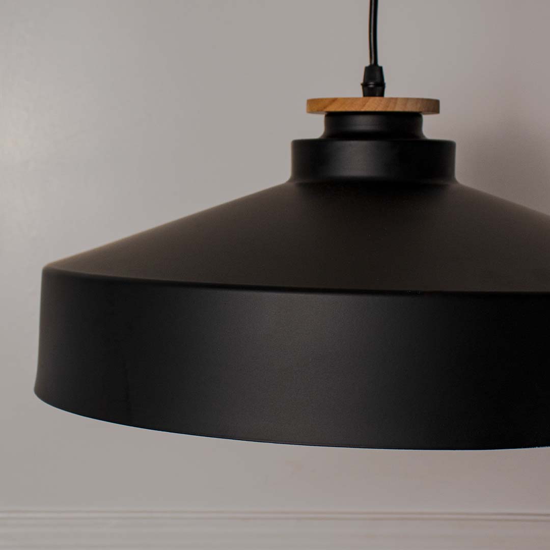 Closeup of matte black dome pendant light with wide metal shade and wooden detail highlighting industrial modern style.