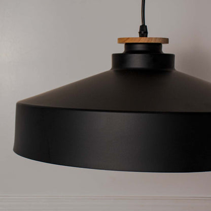 Closeup of matte black dome pendant light with wide metal shade and wooden detail highlighting industrial modern style.