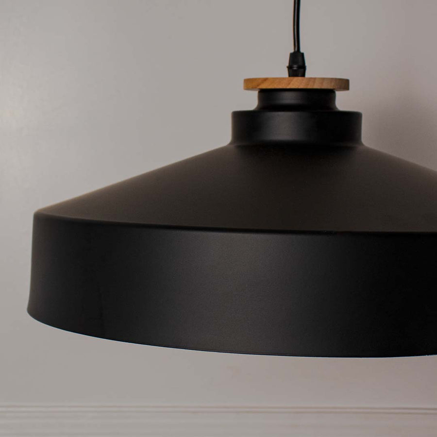 Closeup of matte black dome pendant light with wide metal shade and wooden detail highlighting industrial modern style.