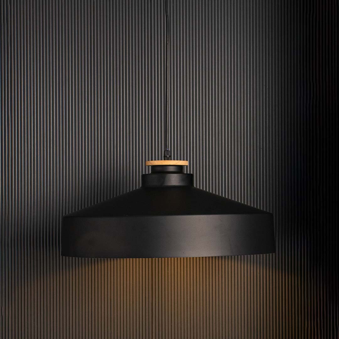 Matte black dome pendant lamp with industrial metal shade and wooden accent glowing warmly on black background decor.