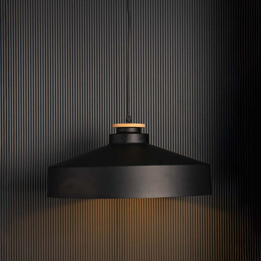 Matte black dome pendant lamp with industrial metal shade and wooden accent glowing warmly on black background decor.