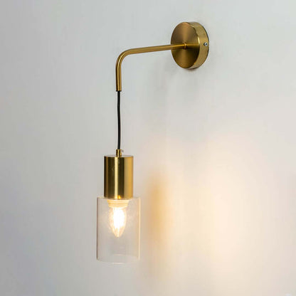 Modern brass wall light with clear glass cylinder shade creating warm elegant interior lighting decor.