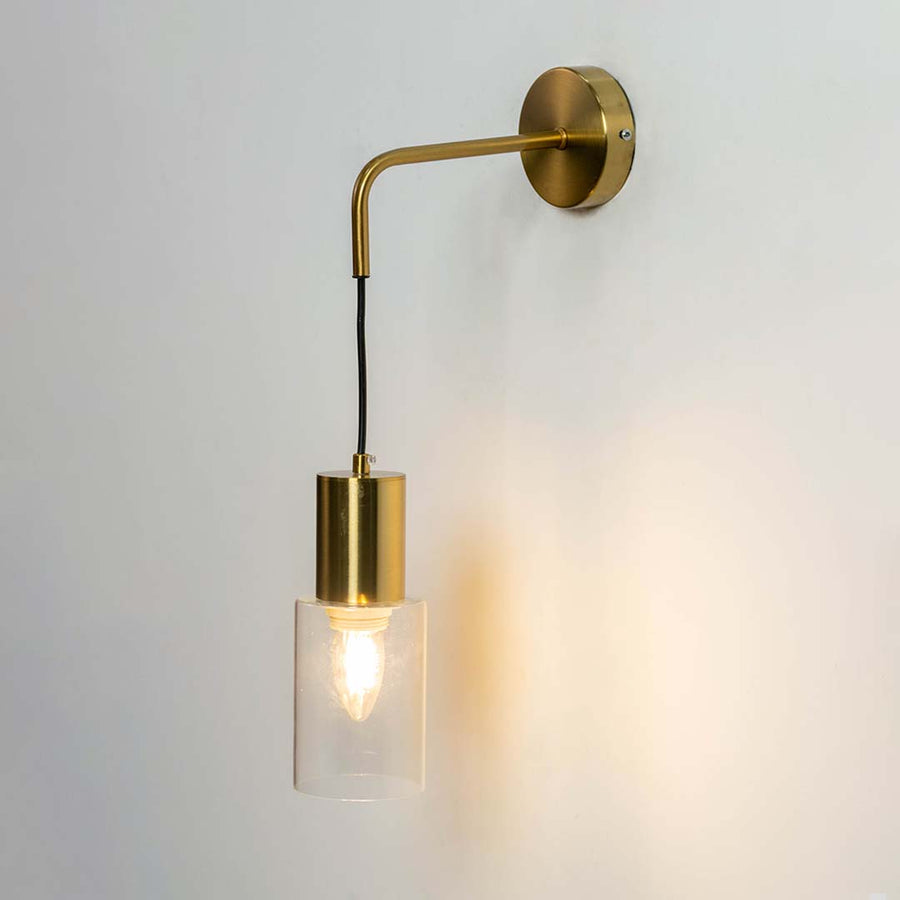 Modern brass wall light with clear glass cylinder shade creating warm elegant interior lighting decor.