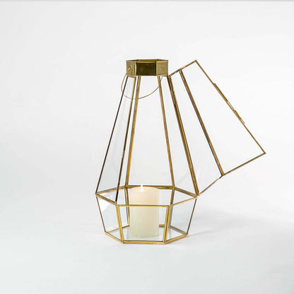 Gold metal and clear glass tapered lantern shown on a white background with candle on highlighting its modern geometric design and warm glow.