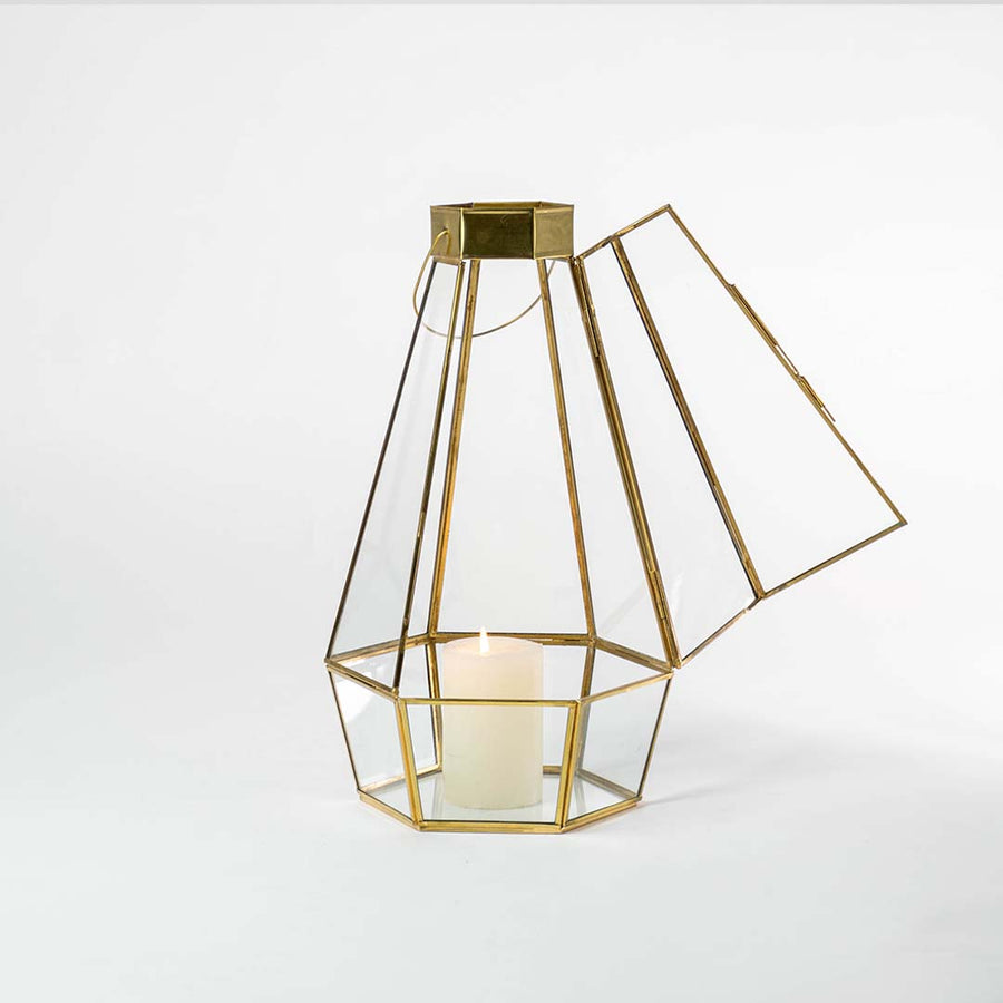 Gold metal and clear glass tapered lantern shown on a white background with candle on highlighting its modern geometric design and warm glow.