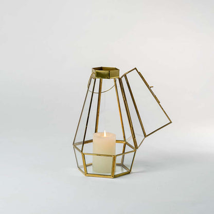 Gold geometric glass candle holder shown on a white background with the candle lit  highlighting its warm glow and clear glass panels.