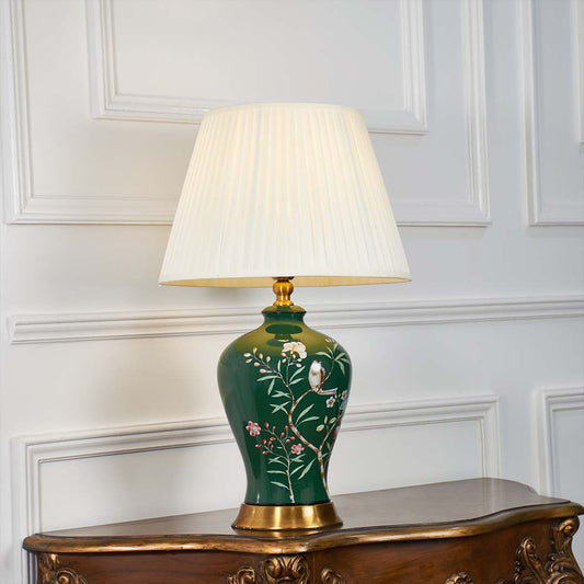 Green ceramic floral table lamp shown with light on against a white background highlighting its warm illumination and artistic hand painted details.