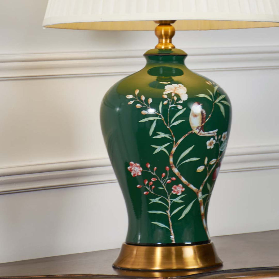 Green floral ceramic table lamp showcasing hand painted bird and botanical detailing with brass base and premium finish.