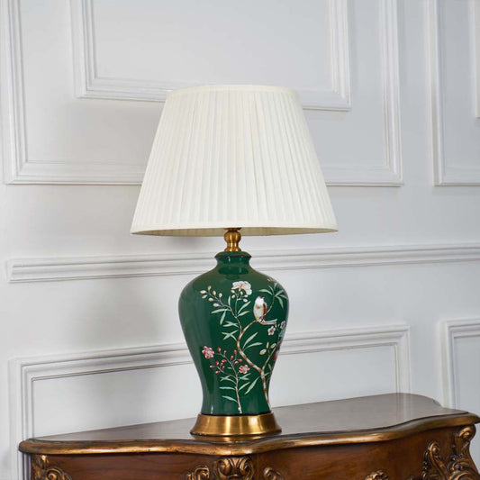 Green ceramic table lamp with floral artwork shown with light off on a white background showcasing its glossy finish and elegant gold base.