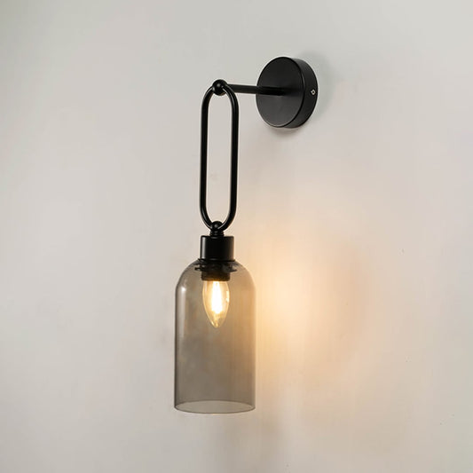 Modern black wall sconce with smoky glass cylindrical shade glowing warm light white background for bedroom and hallway lighting