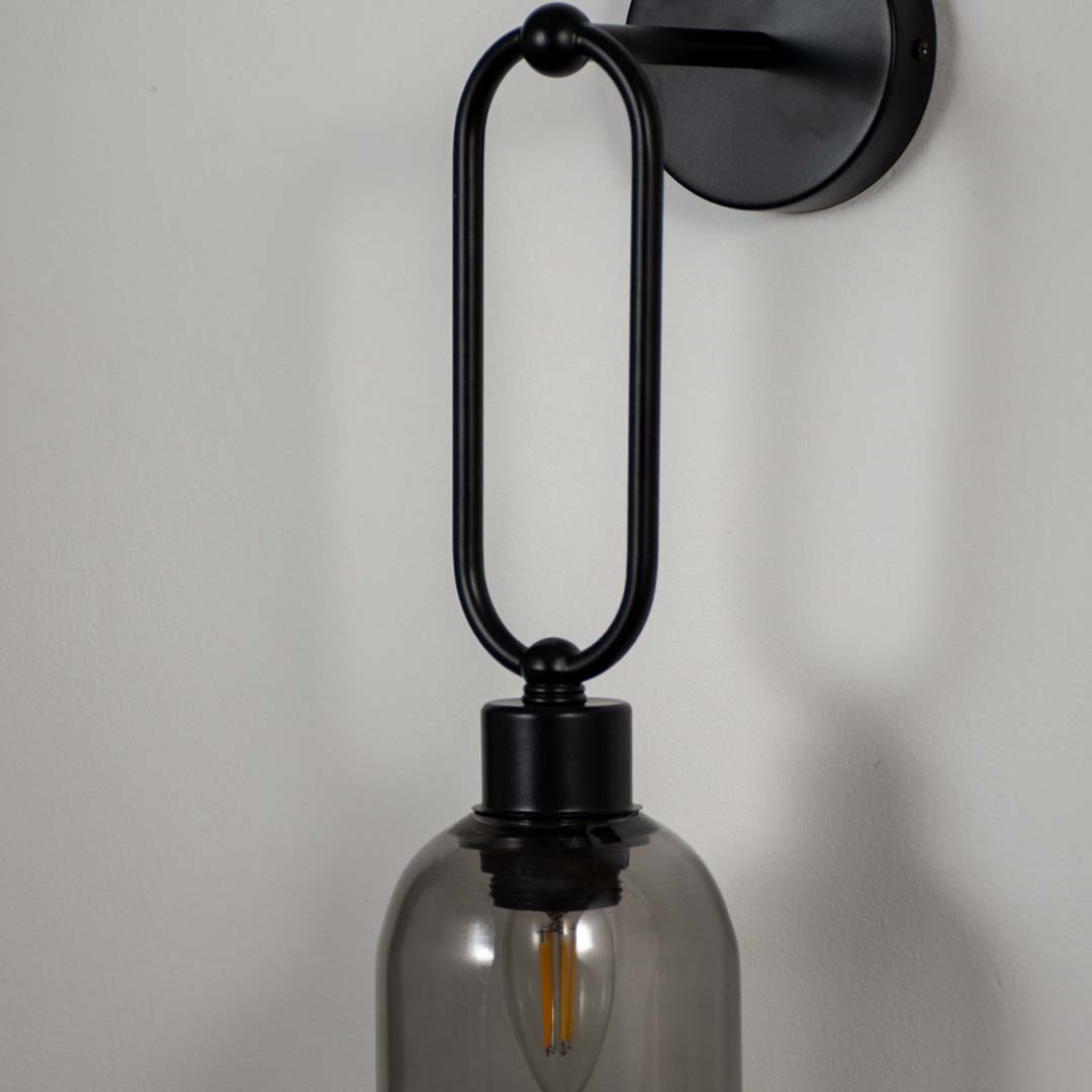 Industrial style black metal wall light with exposed glass bulb mounted on white wall background ideal for modern loft or studio lighting.