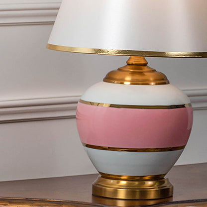 Closeup of pink ceramic table lamp with gold detailing and white shade showing elegant design for modern home lighting decor.