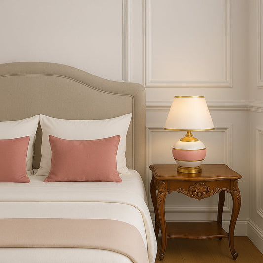 Pink ceramic table lamp with gold accents and white shade glowing on bedside table for elegant bedroom lighting decor.