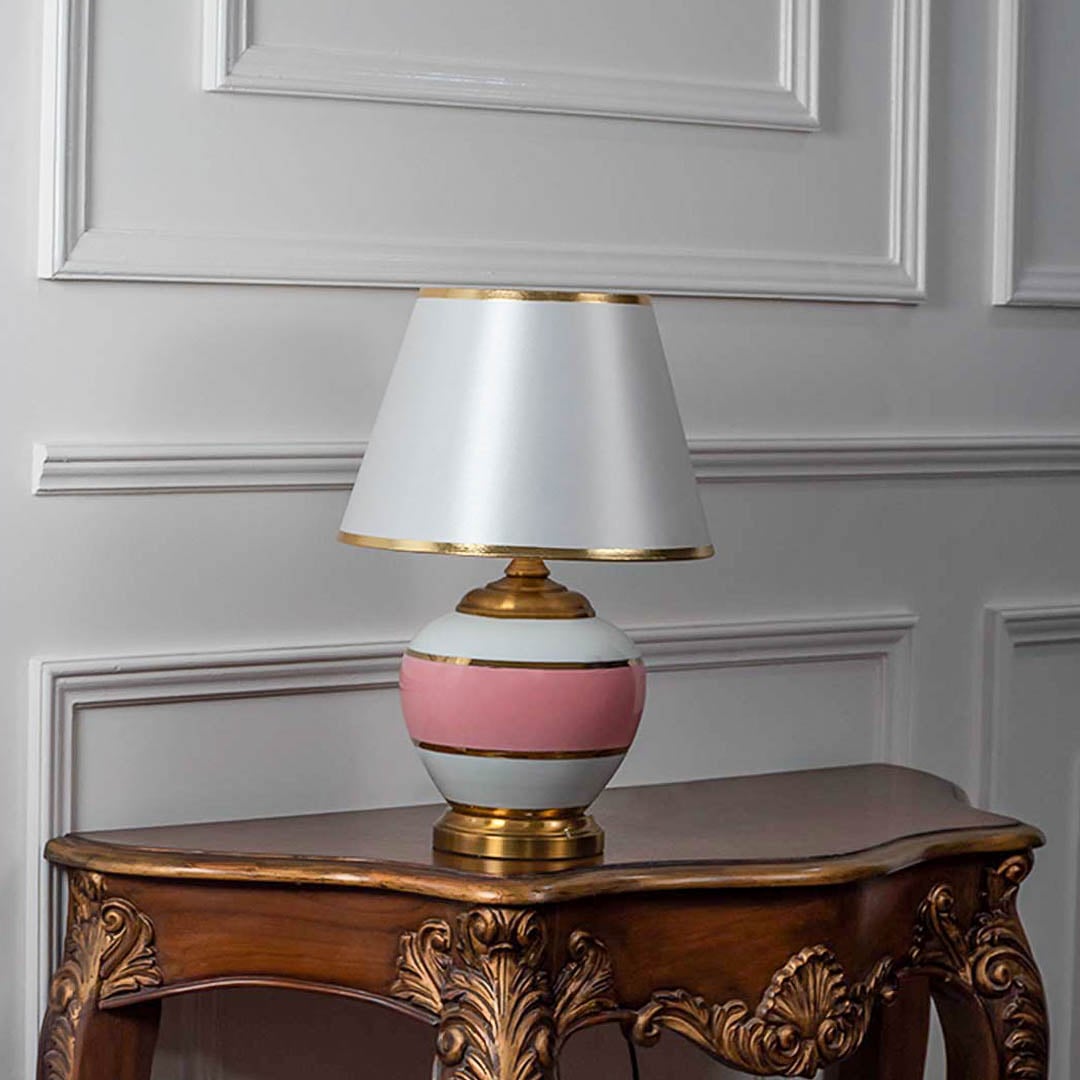 Pink ceramic table lamp with gold accents and white shade switched off on white background for minimalist home lighting design.