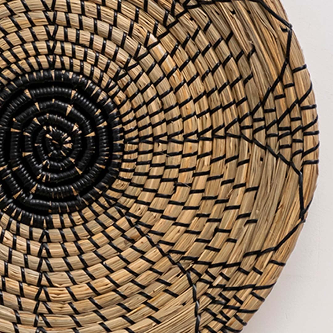 Closeup view of dark woven wall basket with black and brown natural fibers emphasizing deep spiral pattern and textured craftsmanship.