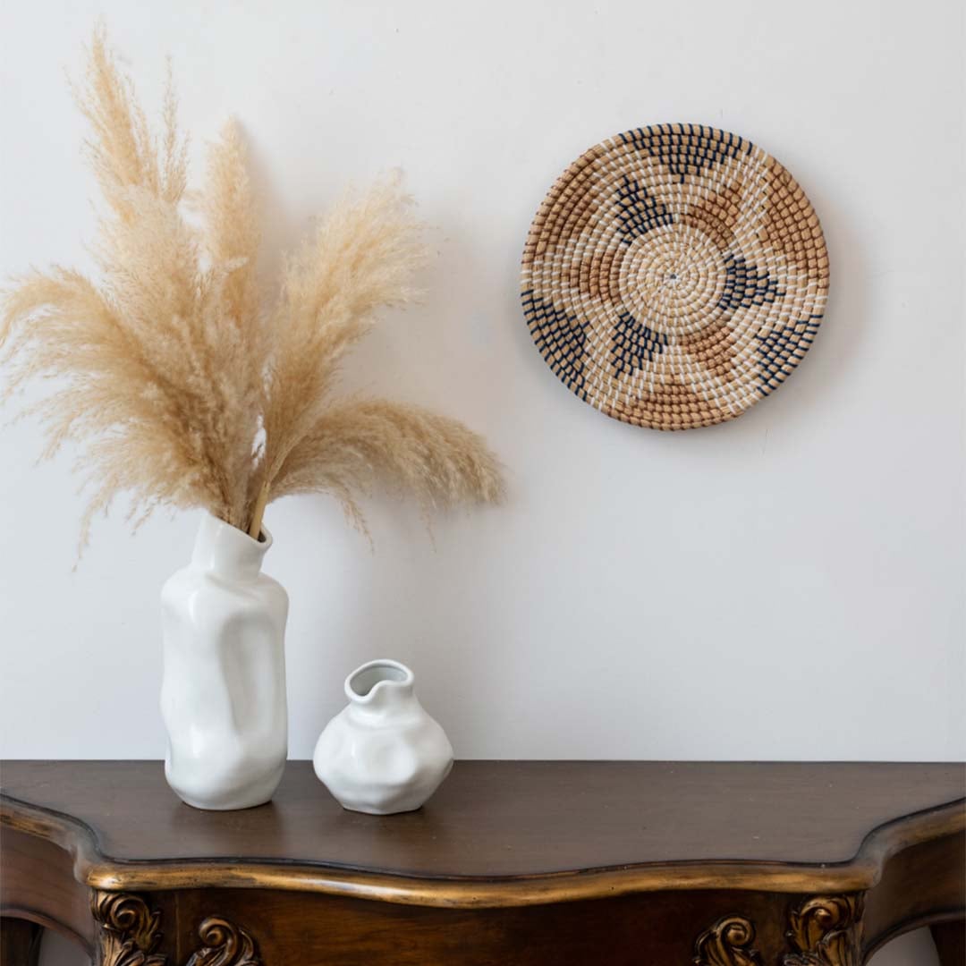 Handwoven wall basket decor styled with vases on wooden console table for rustic boho living room wall.