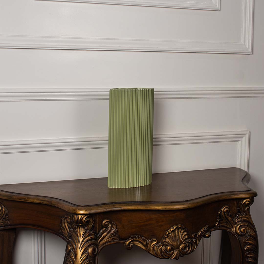 Green ribbed ceramic vase placed on an antique wooden console table against a white paneled wall in a classic luxury interior setting.