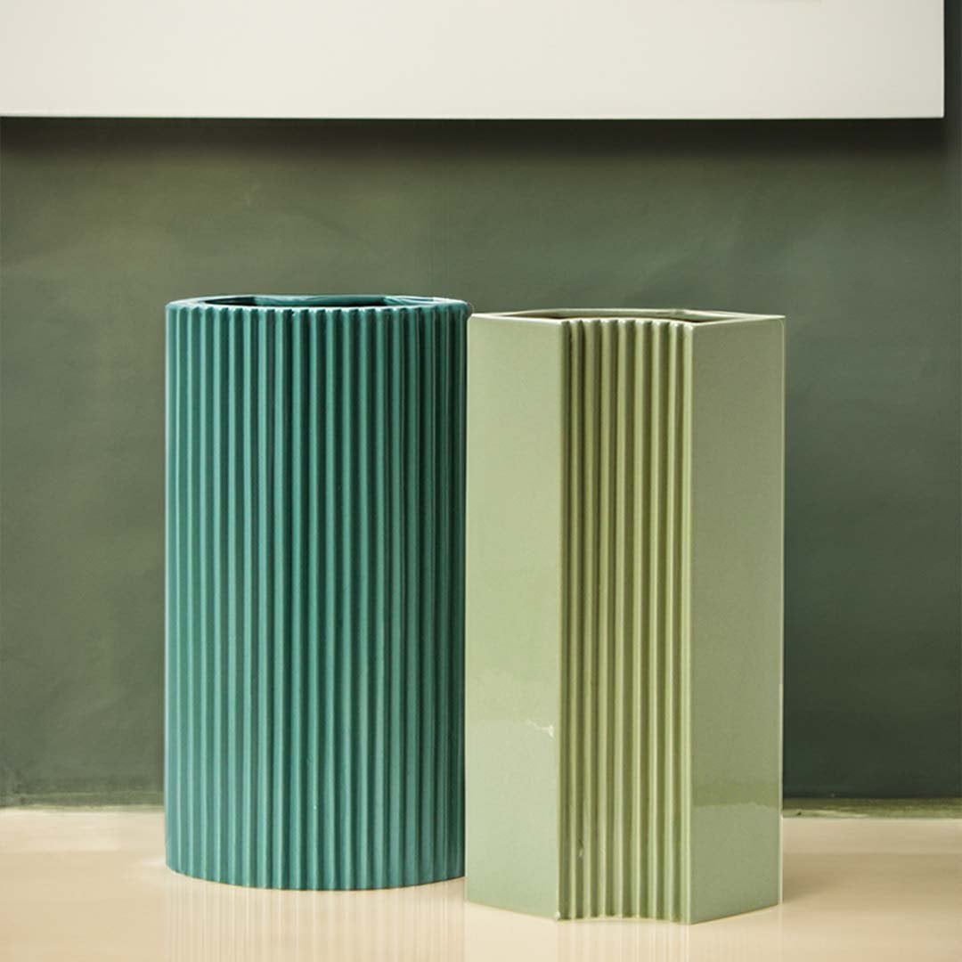 Set of modern teal ceramic vases with linear ridges and soft matte surface displayed against a green backdrop.