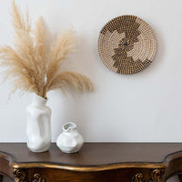 Handwoven wall basket decor in natural and black fiber styled above console table with vases for boho wall.