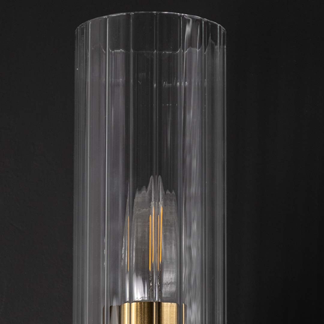 A detailed closeup view of the gold wall light showing the ribbed clear glass shade and polished metal arm with the bulb glowing softly creating a warm ambient effect.