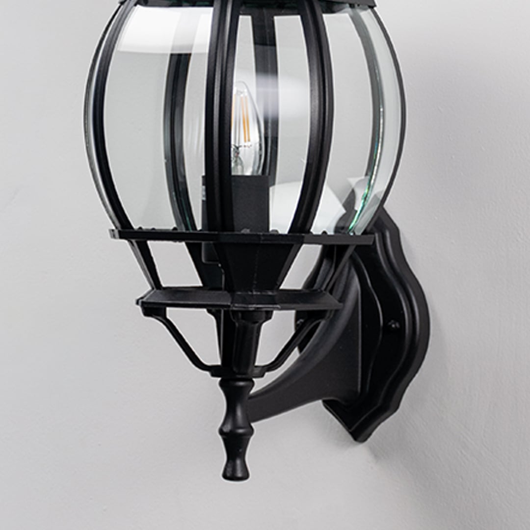 Closeup of black upward wall lantern showing curved glass cage panels and ornate finial detail vintage coach light design.