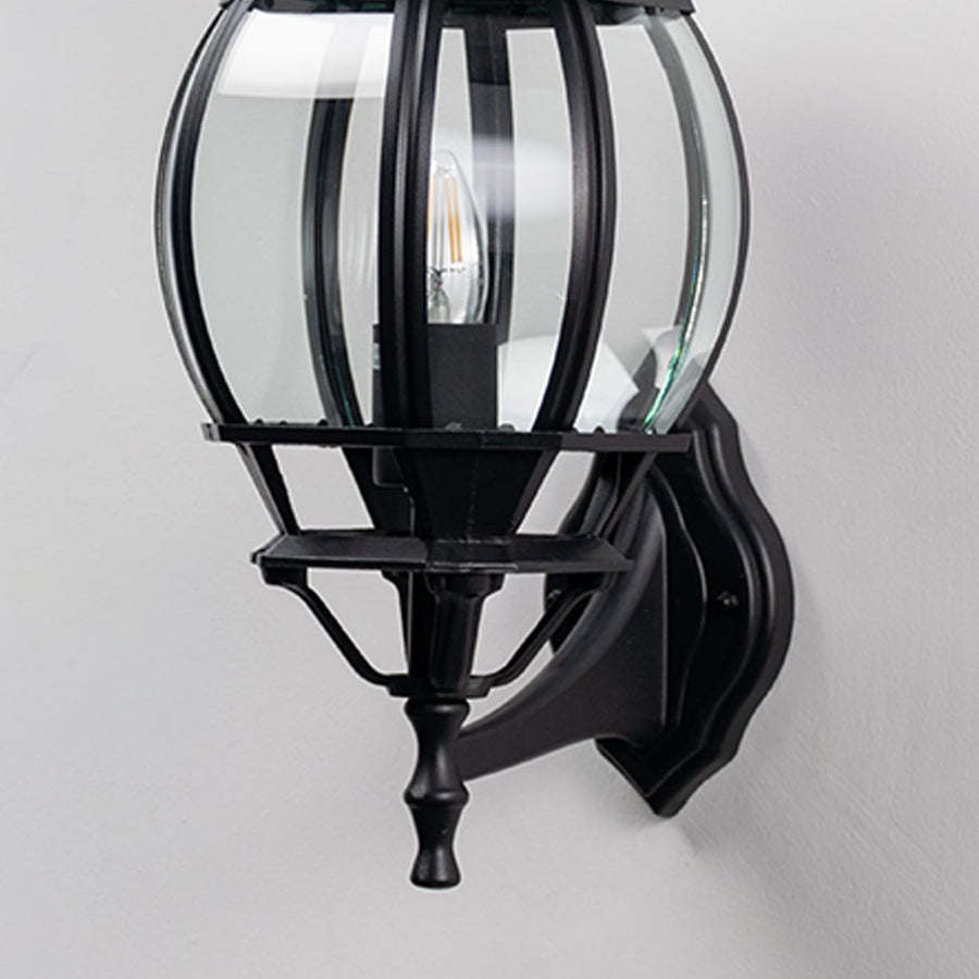 Closeup of black upward wall lantern showing curved glass cage panels and ornate finial detail vintage coach light design.