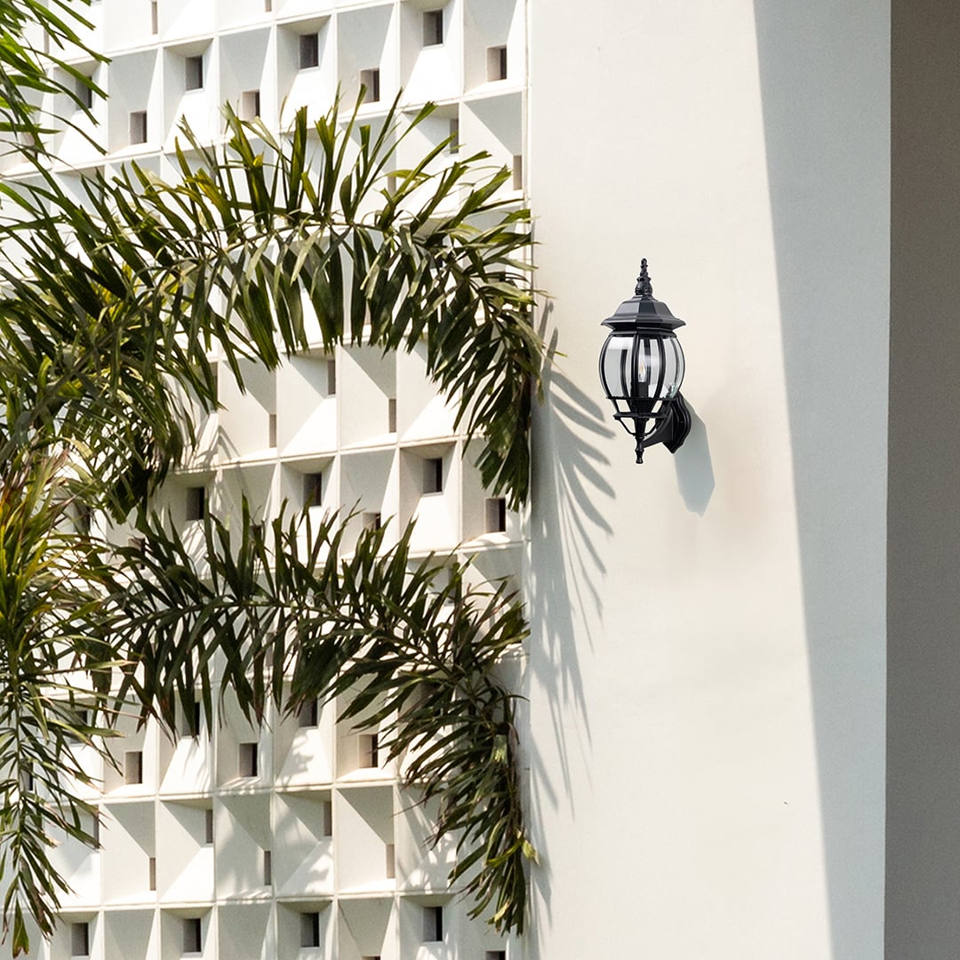 Black outdoor wall sconce with decorative finial lit porch creating traditional vintage coach style exterior lighting.
