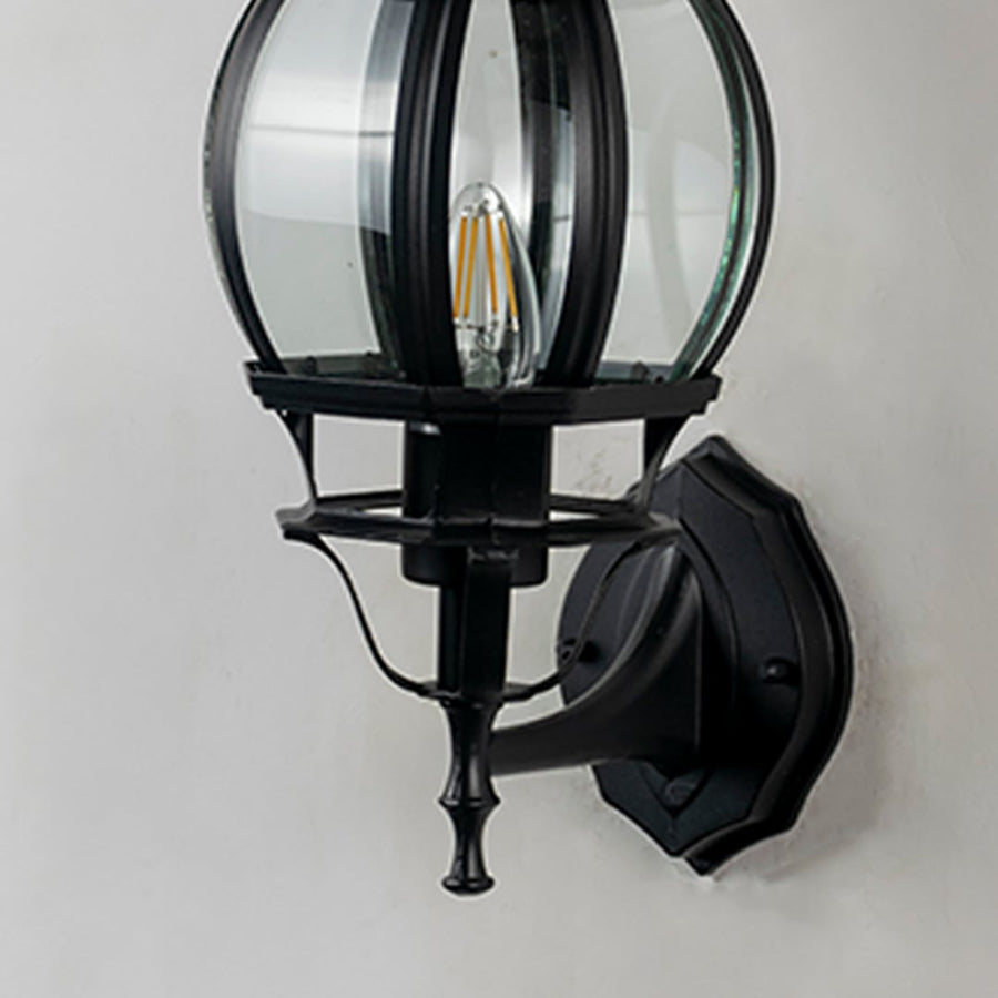 Closeup of black outdoor wall lantern showing curved glass cage panel detail and decorative finial traditional coach design.