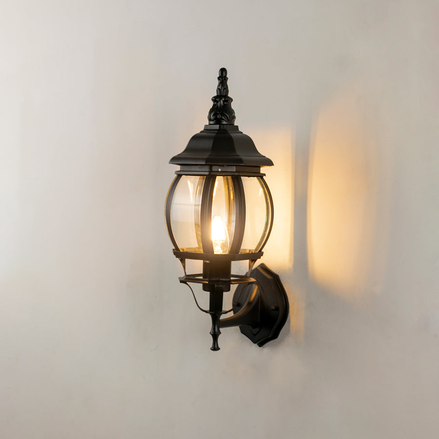 Black metal outdoor wall light on white background with warm glow for stylish exterior entryway decor.