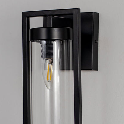 Closeup of black rectangular wall lantern with clear cylindrical glass shade highlighting exposed filament bulb design.