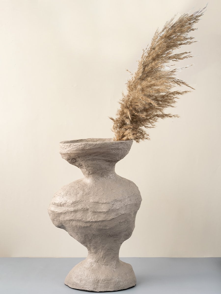 Beige ceramic sculptural vase with textured surface styled with pampas grass for modern home decoration.