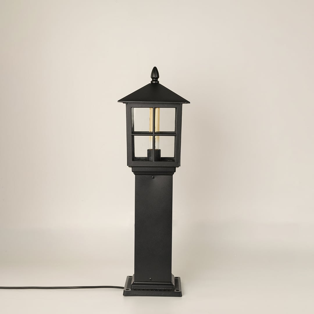 Black outdoor pillar lamp with clear glass shown with light off on a white background displaying its structured frame and elegant outdoor form.
