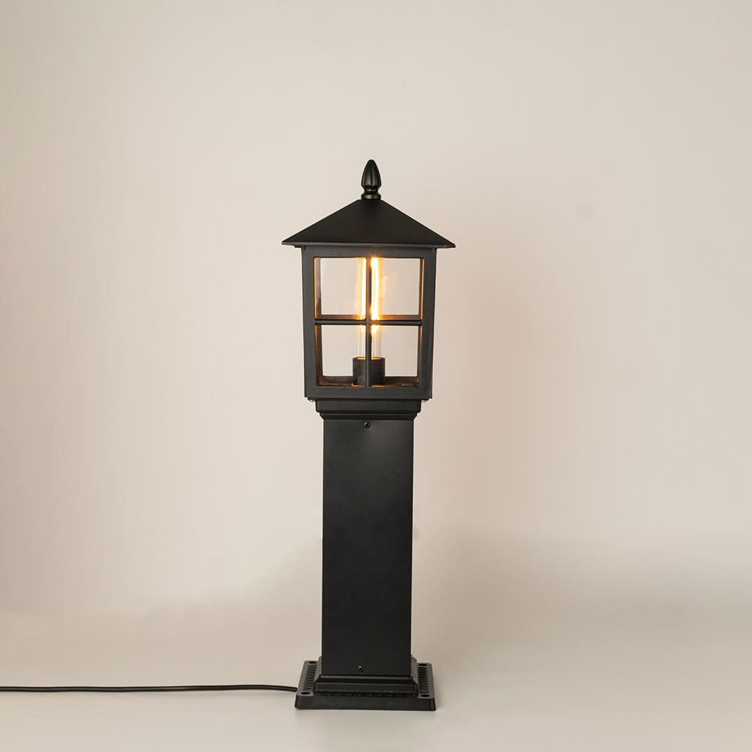 Modern black outdoor bollard light with warm glowing bulb for elegant exterior decor styling use.