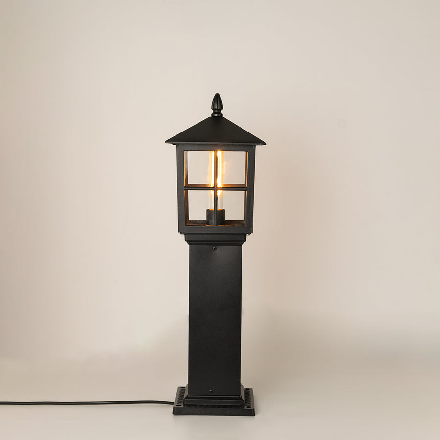 Modern black outdoor bollard light with warm glowing bulb for elegant exterior decor styling use.