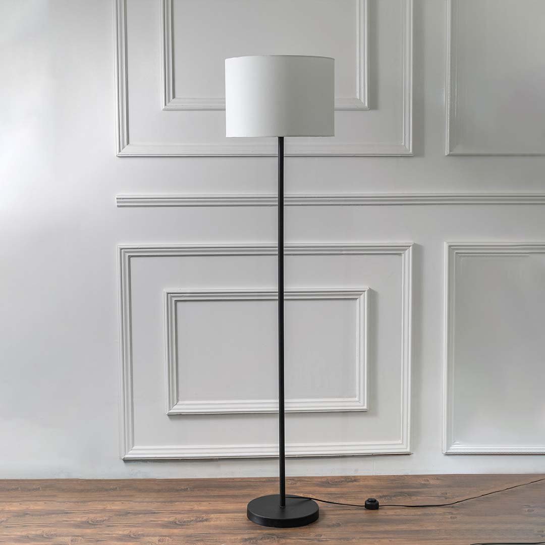 Black metal floor lamp with white fabric drum shade and round base for modern living room and bedroom decor.