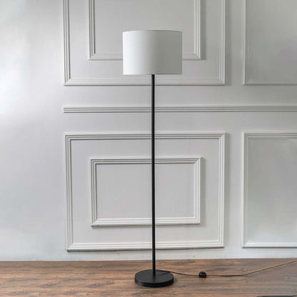 Black metal floor lamp with white fabric drum shade and round base for modern living room and bedroom decor.