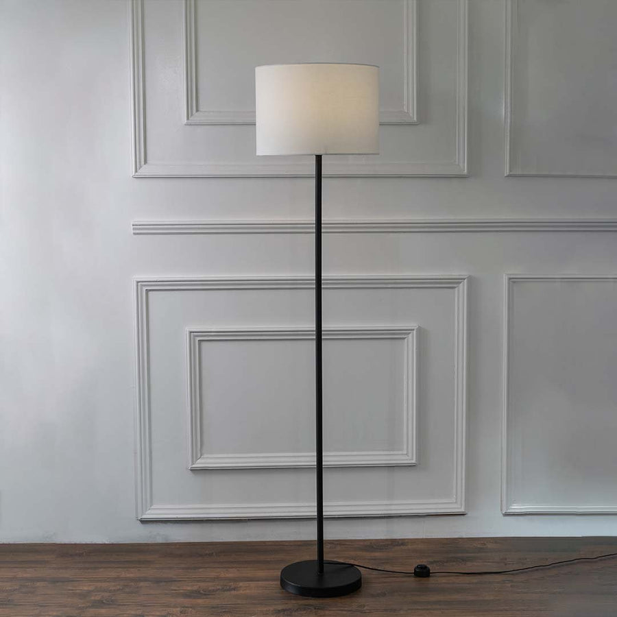Minimalist black floor lamp with white fabric shade and round base for modern interior and reading corner styling.