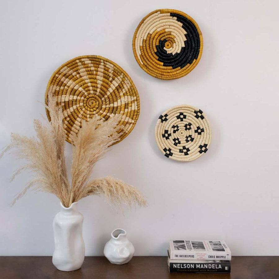 Main lifestyle view of woven wall basket with black white and mustard spiral design styled on wall with vases and pampas grass.