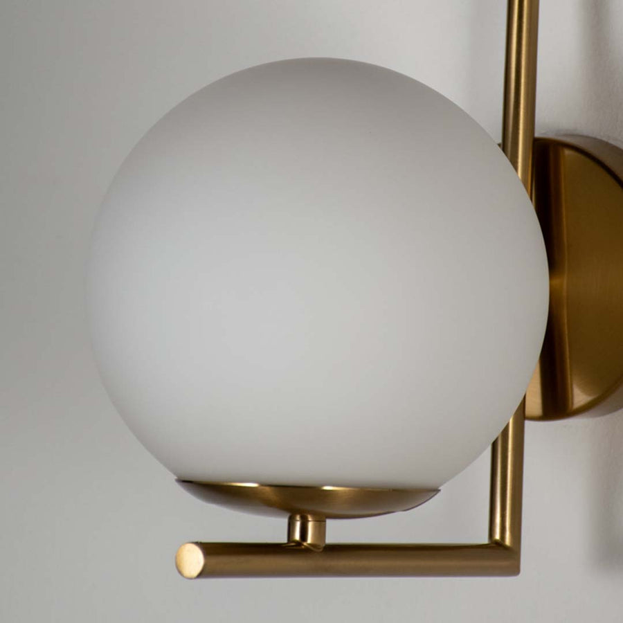 Close up wall light with white glass globe and gold frame on neutral background minimal modern lighting for home decor.