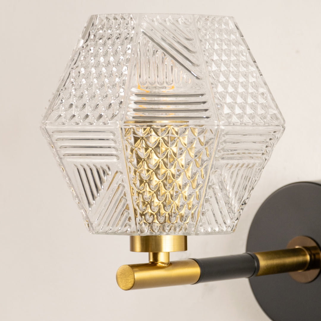 Closeup of gold metal wall light with geometric glass shade showcasing intricate pattern and premium finish for modern decor styling.